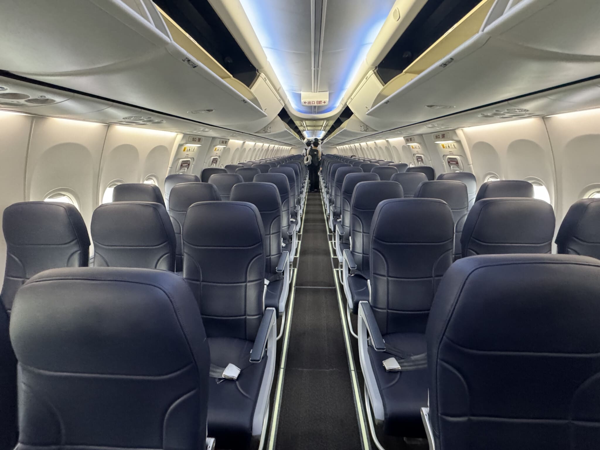 View along an aircraft cabin aisle with passenger seating and overhead panels