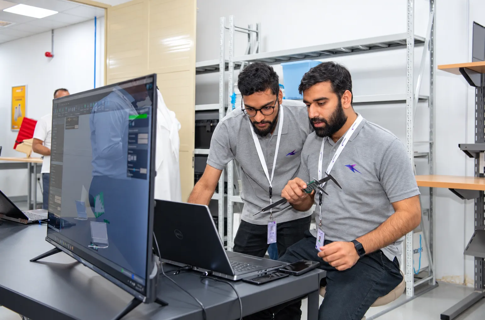 Two engineers with callipers reviewing a part on screen